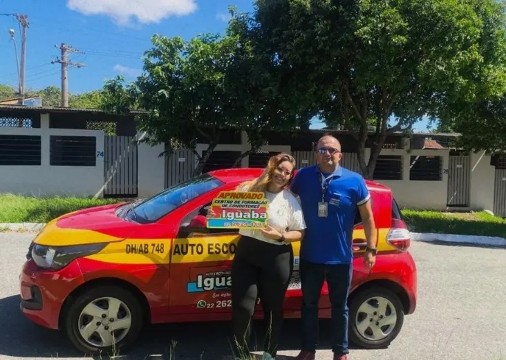 Aluna aprovada na categoria B com o instrutor, ao lado do carro vermelho da Auto Escola Iguaba